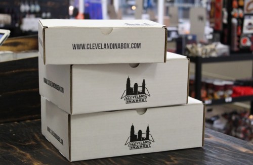 Three stacked white boxes with "Cleveland in a Box" logo and website displayed on a wooden table.