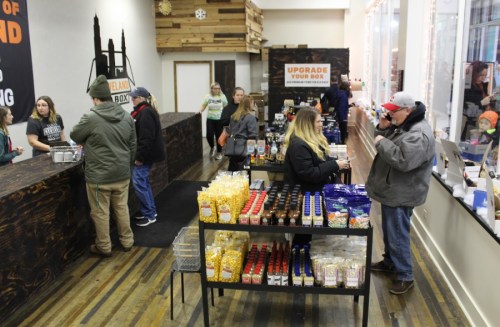 A busy store interior with customers at the counter and shelves displaying various food products.