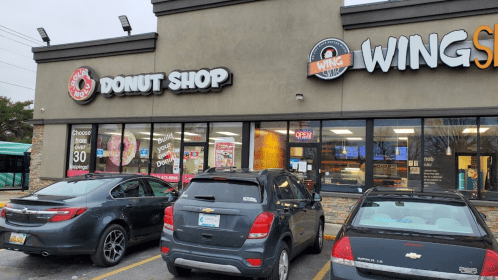 Exterior of a donut shop and wing restaurant, featuring a sign and parked cars in front.