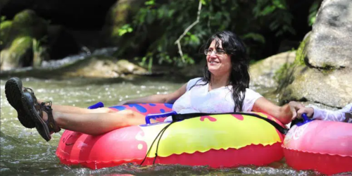 A woman relaxes on a colorful inner tube in a river, enjoying a sunny day outdoors.