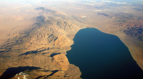 Aerial view of rugged mountains and a large body of water surrounded by arid landscape.