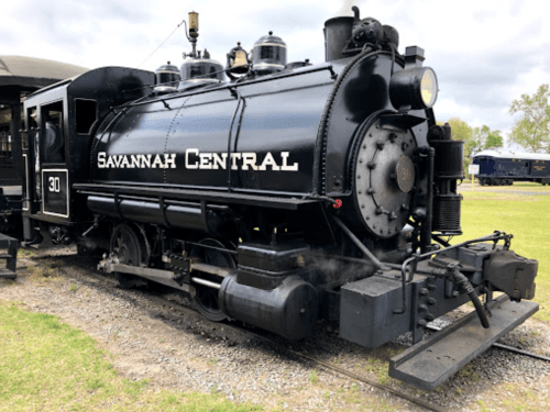 A vintage black steam locomotive labeled "Savannah Central" parked on a grassy area.