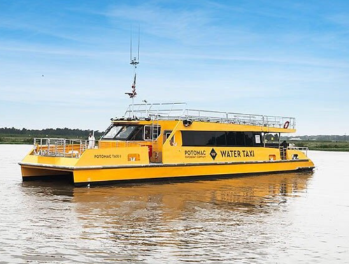 A bright yellow water taxi named "Potomac Water Taxi" floats on calm waters under a clear blue sky.