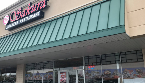 Exterior of Sakura Japanese Restaurant, featuring a green awning and large windows displaying menu items. Sign says "Open."