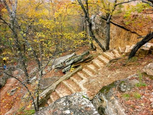 A winding stone staircase surrounded by autumn trees and rocky terrain in a natural setting.