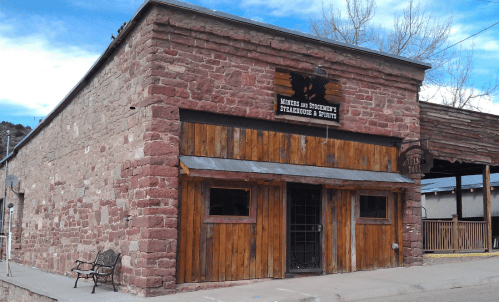 Exterior of a rustic stone building with wooden accents, featuring a sign for a steakhouse and spirits.