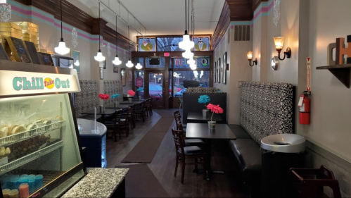 A cozy café interior with patterned booths, tables, and colorful flowers, featuring a display case and warm lighting.