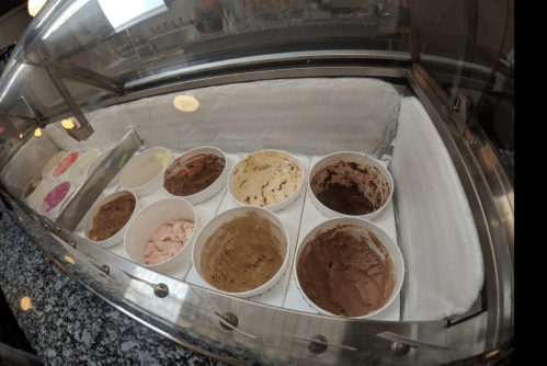 A display of various ice cream flavors in tubs, set in a glass case with a granite countertop.