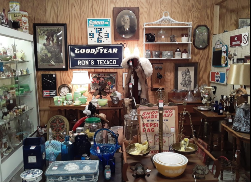 A cozy antique shop filled with vintage items, including glassware, signs, and collectibles on wooden shelves and tables.