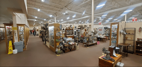 A spacious antique store aisle filled with various vintage items and displays, with shoppers in the background.
