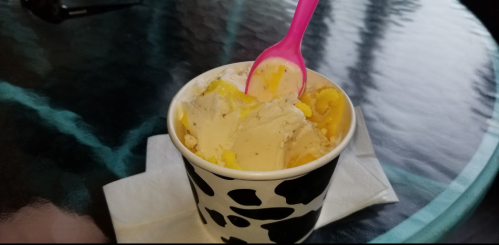 A cup of ice cream with a pink spoon, sitting on a table with a cow print design.