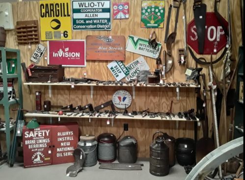 A collection of vintage signs, tools, and memorabilia displayed on shelves and walls in a rustic setting.