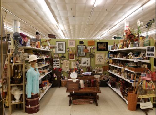 A vintage shop aisle filled with various antiques, decorations, and clothing on shelves and tables.