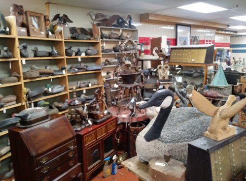 A collection of antique decoys and wooden carvings displayed on shelves and tables in a shop.