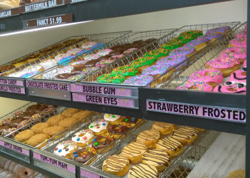 A display of colorful donuts, including bubble gum, strawberry frosted, and various frosted varieties with sprinkles.