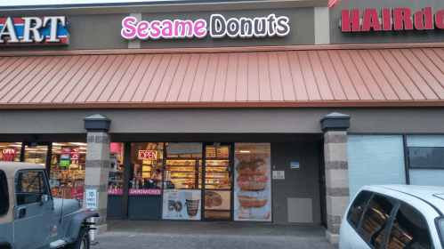 Storefront of Sesame Donuts with a bright "OPEN" sign and a display of donuts in the window.