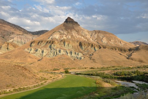 A scenic landscape featuring a prominent mountain peak, rolling hills, and a winding river surrounded by greenery.