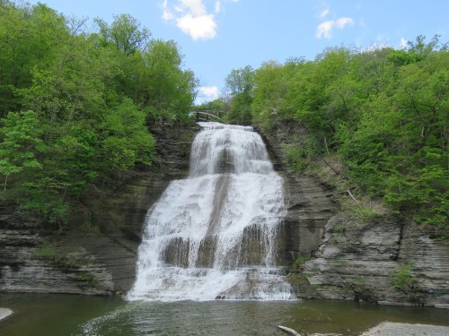 A cascading waterfall surrounded by lush green trees under a blue sky.
