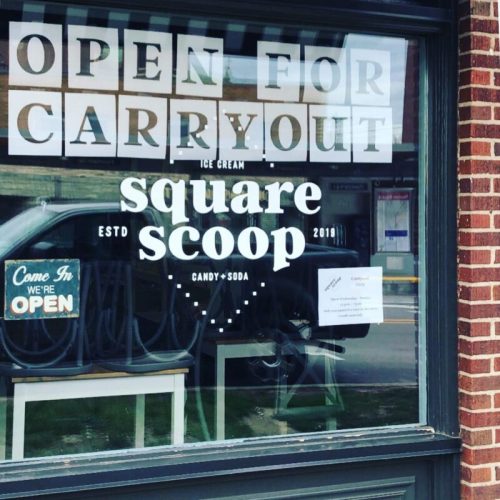 Window display of Square Scoop ice cream shop, featuring "Open for Carryout" sign and details about their offerings.