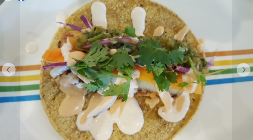 A colorful taco topped with fresh cilantro, vegetables, and drizzled with sauce on a corn tortilla.