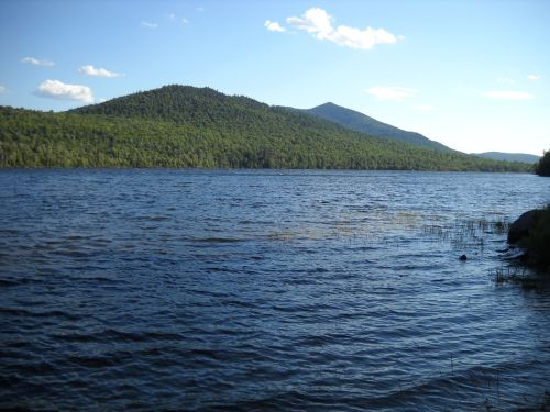 A serene lake surrounded by lush green mountains under a clear blue sky with a few clouds.