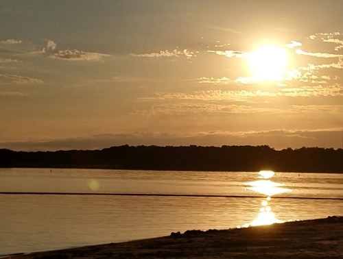 Sunset over a calm river, with golden reflections on the water and silhouettes of trees in the background.