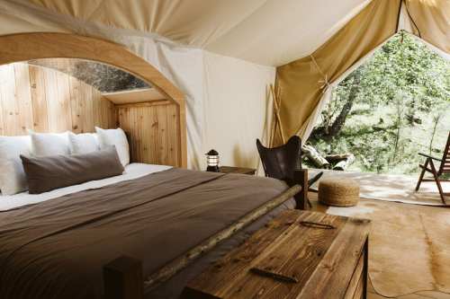 Cozy glamping tent interior with a wooden bed, lantern, and outdoor view of nature.