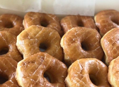 A close-up of a box filled with freshly glazed donuts arranged neatly.
