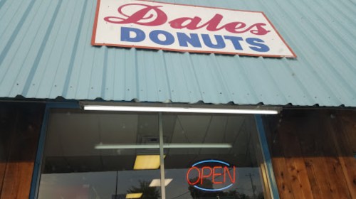 Sign for "Dale's Donuts" with an illuminated "OPEN" sign in the window of a blue building.