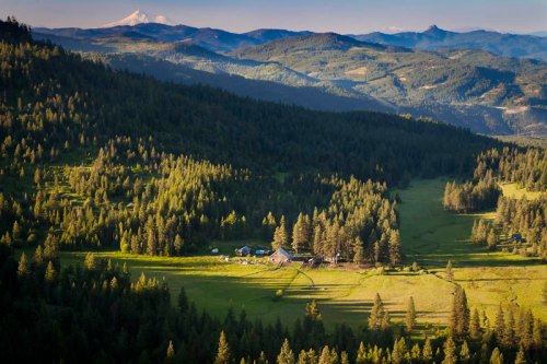 A scenic view of a lush green valley surrounded by mountains and forests, with a small farm nestled in the landscape.