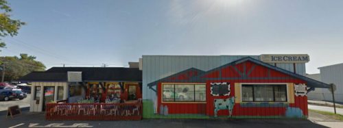 Colorful ice cream shop with a red and blue exterior, outdoor seating, and a mural of a cow on the wall.