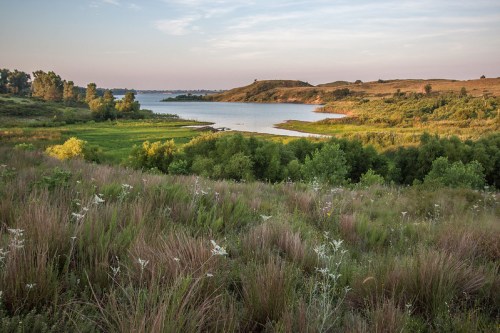 A serene landscape featuring a lake surrounded by lush greenery and rolling hills under a clear sky.