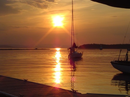 A serene sunset over calm waters, with a sailboat silhouetted against the glowing horizon.