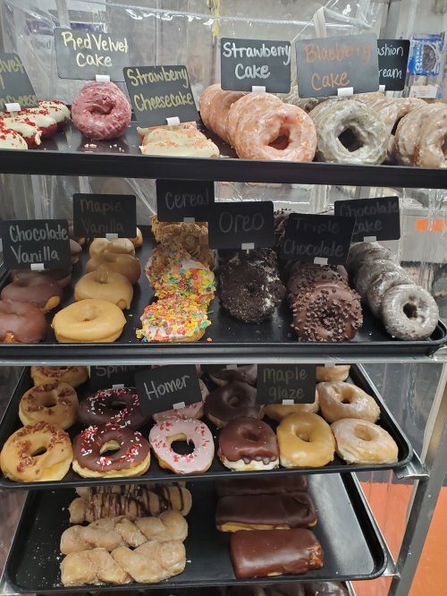 A display of assorted donuts with labels, including flavors like red velvet, strawberry, blueberry, and chocolate.