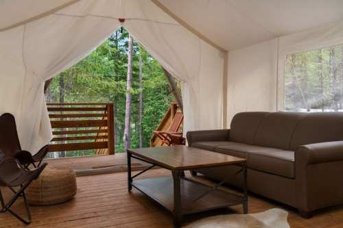 Cozy tent interior with a sofa, coffee table, and views of trees through an open entrance.