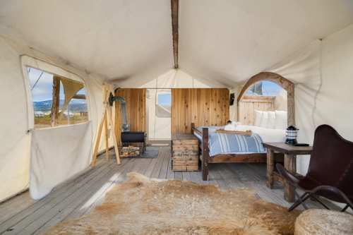 Cozy glamping tent interior with a wooden bed, rustic decor, and a view of nature through large windows.