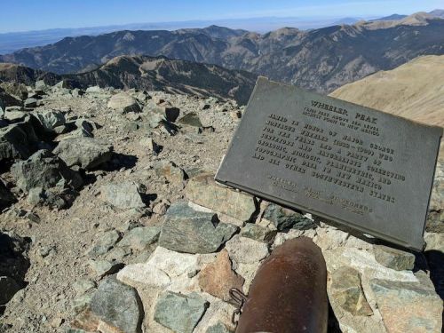A plaque on rocky terrain at Wheeler Peak, with mountains in the background under a clear blue sky.