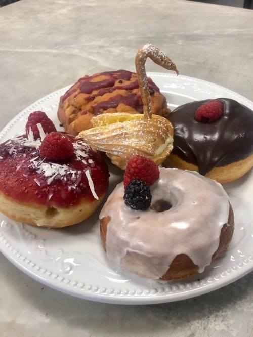 A plate of assorted donuts, including glazed, chocolate, and fruit-topped varieties, garnished with raspberries.