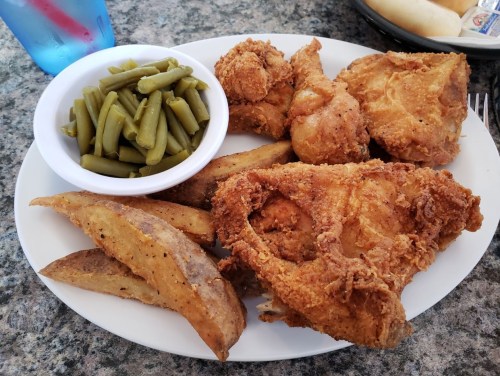 A plate of fried chicken, seasoned potato wedges, and green beans on a granite table. A blue drink is in the background.