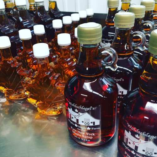 Bottles of maple syrup in various shapes, arranged on a table, showcasing rich amber color and labels.