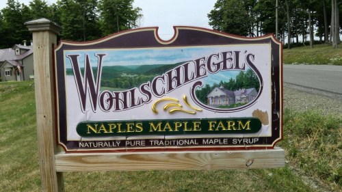 Sign for Wohlschlegel's Naples Maple Farm, featuring a scenic landscape and text about traditional maple syrup.