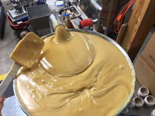 A large bowl filled with creamy, light brown mixture being poured from a spout, with a spatula resting on the edge.