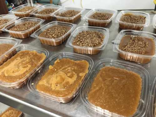 Containers of caramel or fudge topped with crushed nuts, arranged on a metal surface.