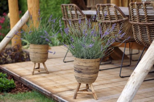 Two wicker planters with lavender sit on a wooden deck beside a dining table and chairs.
