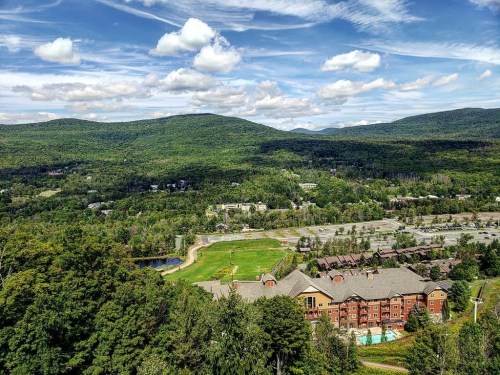 A scenic view of mountains and a resort surrounded by lush greenery under a partly cloudy sky.