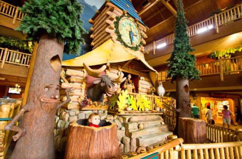 A whimsical log cabin display with trees, a clock, and playful animal figures in a lodge setting.