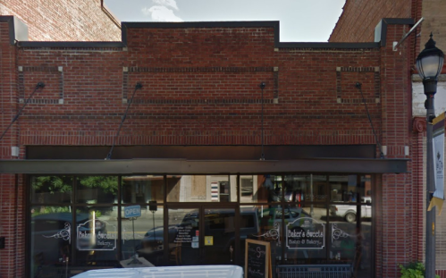 A brick storefront with large windows and an "OPEN" sign, featuring a bakery and café.