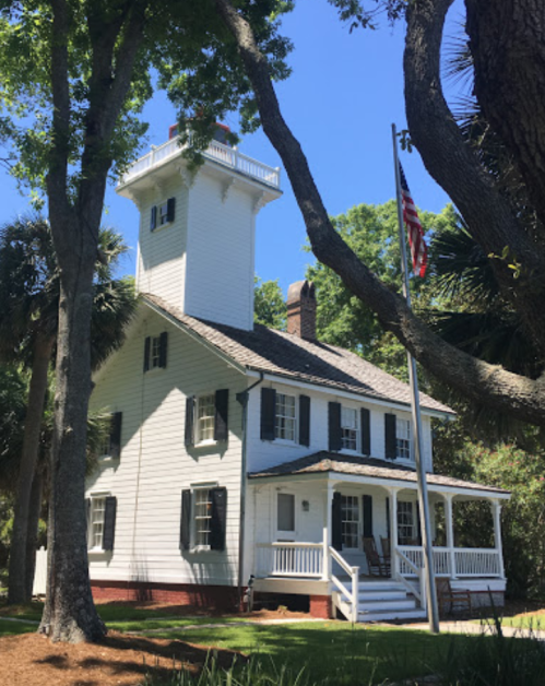 A white two-story house with a lighthouse tower, surrounded by trees and featuring an American flag.