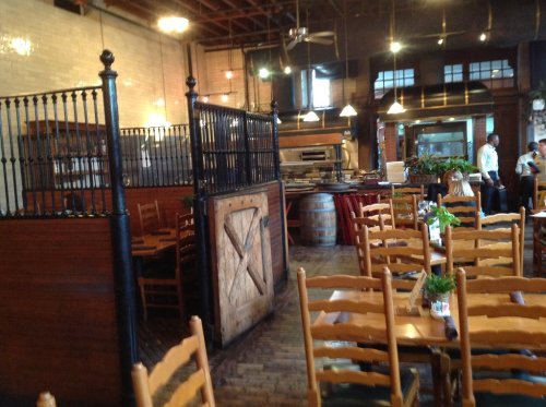 Interior of a rustic restaurant featuring wooden tables, chairs, and an open kitchen area with warm lighting.