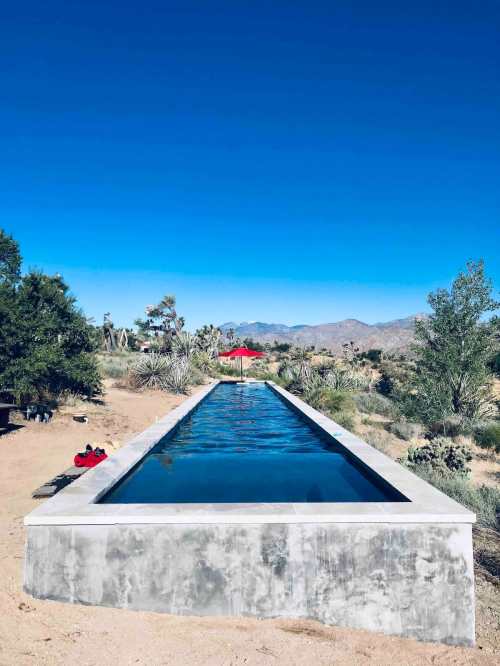 A long, narrow pool surrounded by desert landscape and mountains under a clear blue sky.